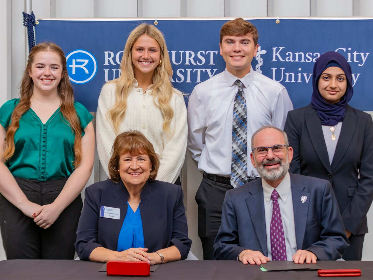 Rockhurst University students stand behind KCU and Rockhurst leaders as agreement is signed.